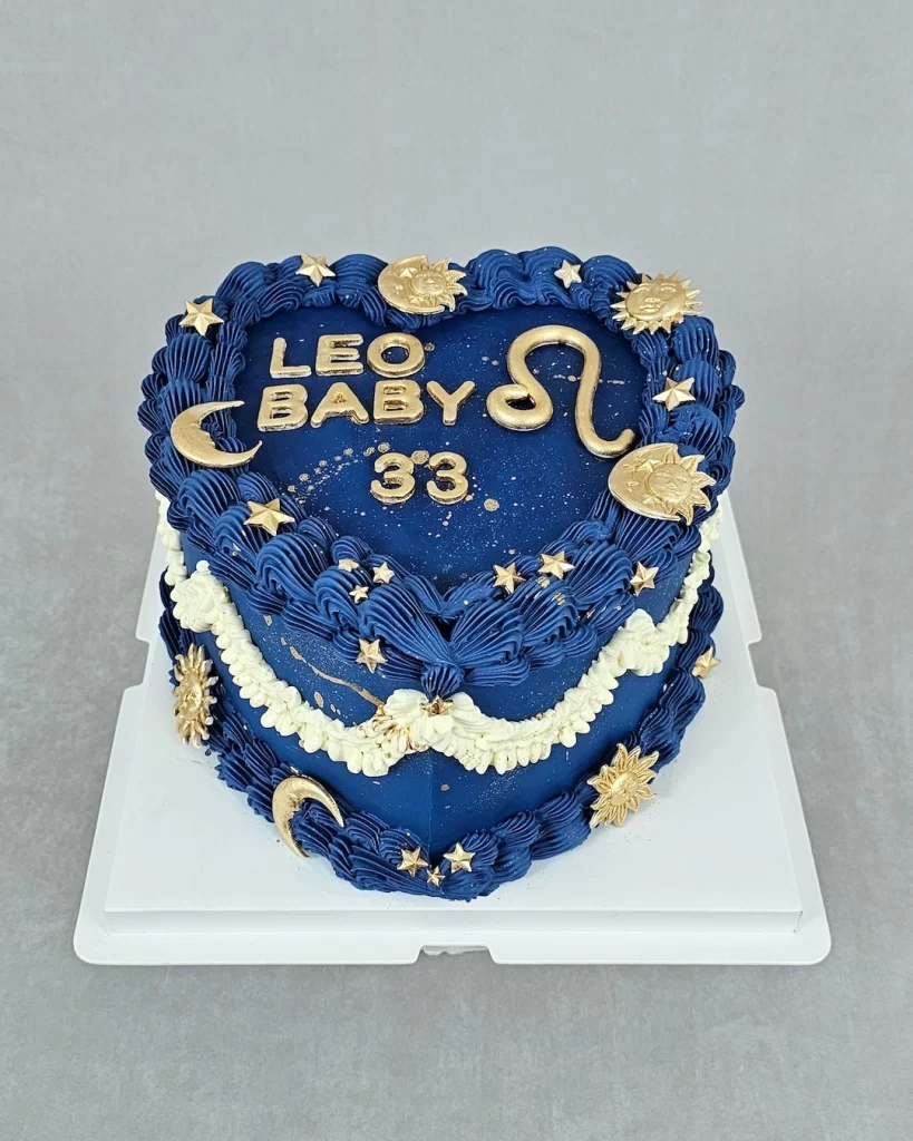 Dark blue heart-shaped cake decorated with zodiac-themed designs and gold accents