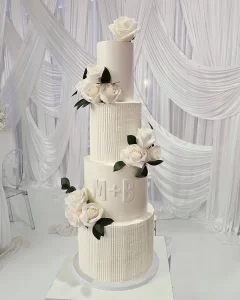 A beautiful four-tier white wedding cake decorated with flowers and personalized initials.