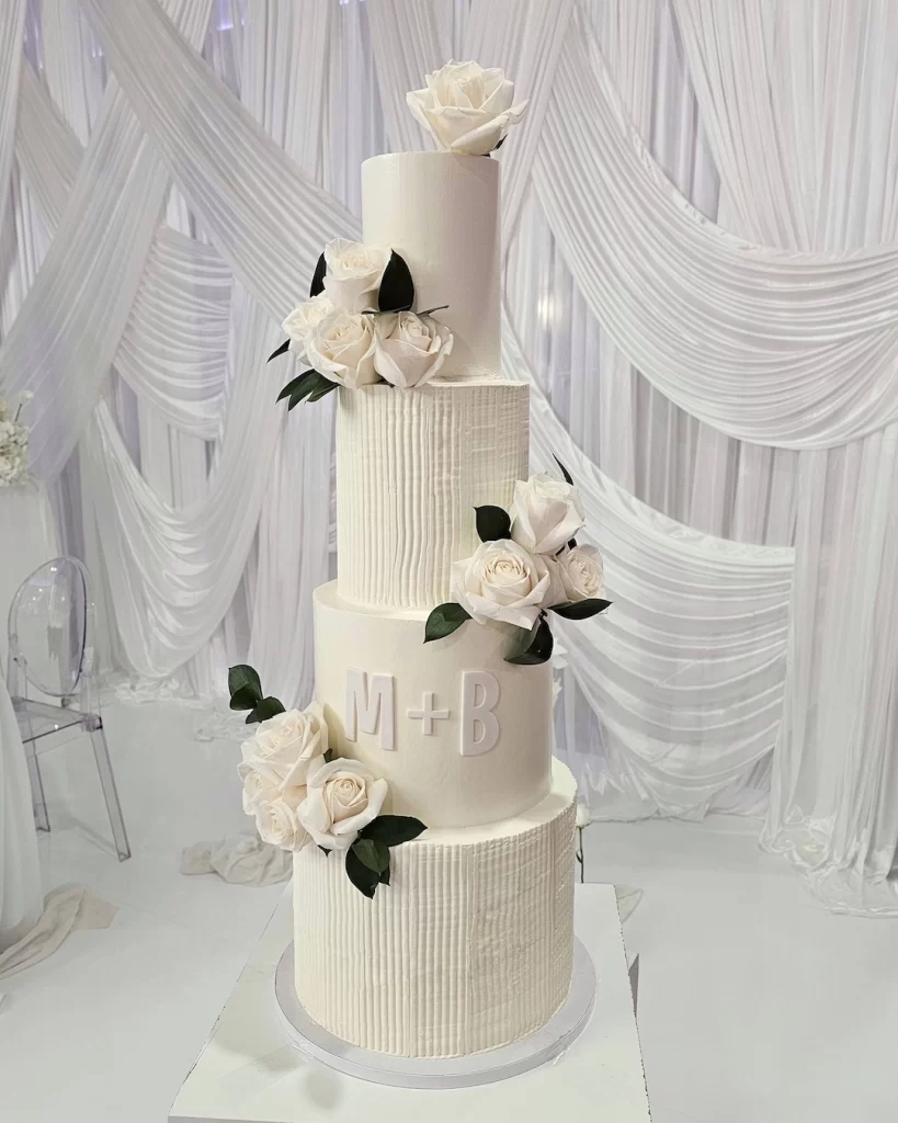 A beautiful four-tier white wedding cake decorated with flowers and personalized initials.