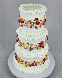 A three-tier wedding cake decorated with colorful buttercream flowers