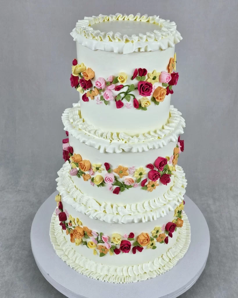 A three-tier wedding cake decorated with colorful buttercream flowers