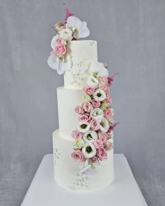 An elegant three-tier wedding cake decorated with fresh flowers and stencil designs