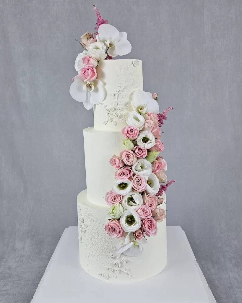 An elegant three-tier wedding cake decorated with fresh flowers and stencil designs