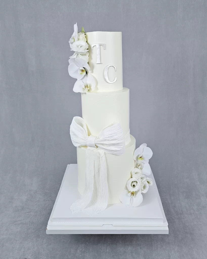 Adorable three-tier white wedding cake decorated with fresh flowers and initials