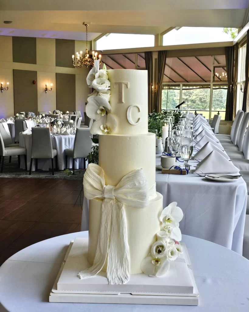 Adorable three-tier white wedding cake decorated with fresh flowers and initials
