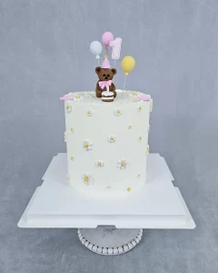 Beautiful white birthday cake decorated with a cute bear and colorful balloons