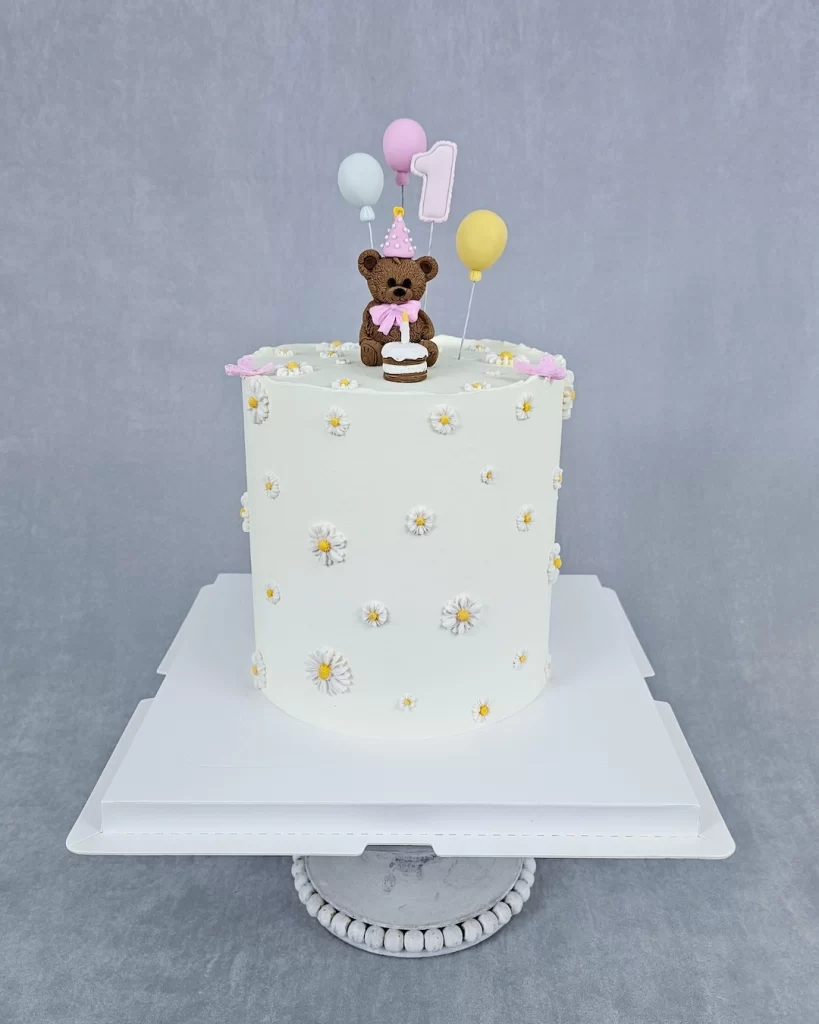 Beautiful white birthday cake decorated with a cute bear and colorful balloons