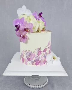 A white wedding cake decorated with fresh orchids and buttercream art