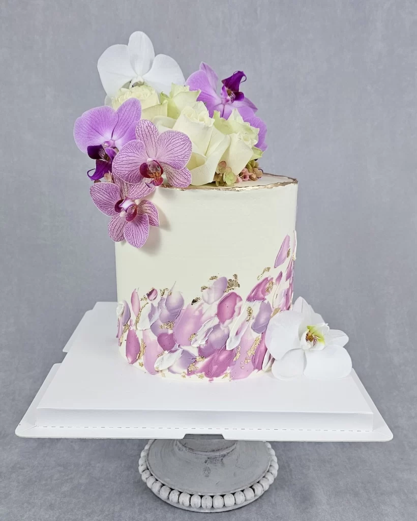 A white wedding cake decorated with fresh orchids and buttercream art
