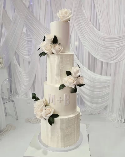 A beautiful four-tier white wedding cake decorated with flowers and personalized initials.