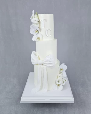 Adorable three-tier white wedding cake decorated with fresh flowers and initials