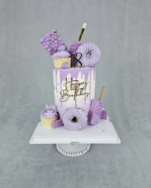 A tall white and purple birthday cake decorated with donuts, cupcakes, ice cream, and chocolate
